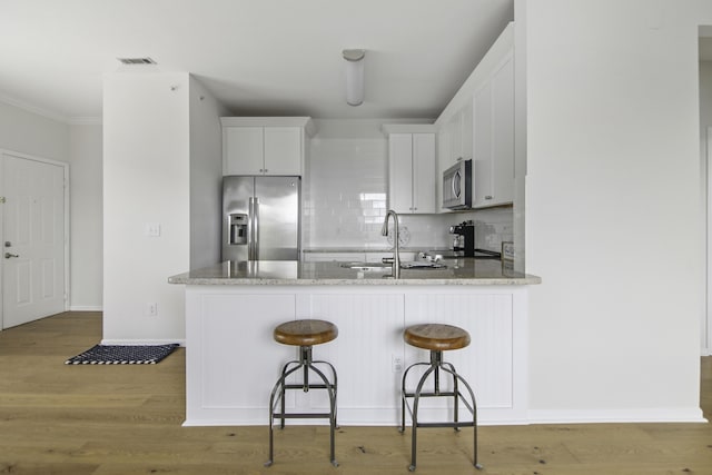 kitchen with a breakfast bar area, stainless steel appliances, visible vents, white cabinetry, and a sink