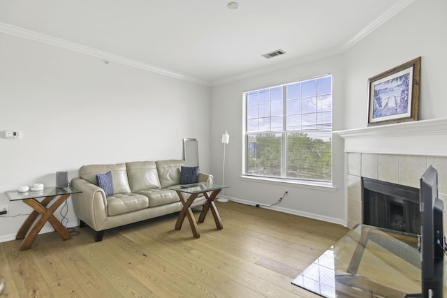 living room with light wood-type flooring, a fireplace, visible vents, and crown molding