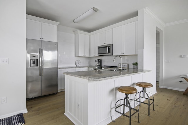 kitchen featuring wood finished floors, a sink, white cabinetry, appliances with stainless steel finishes, and decorative backsplash