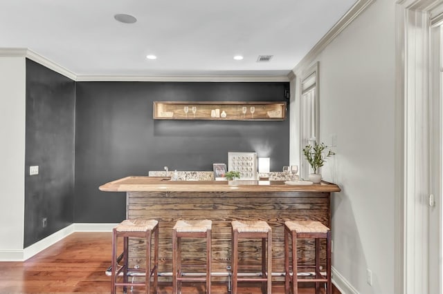 bar featuring visible vents, wood finished floors, indoor bar, and ornamental molding