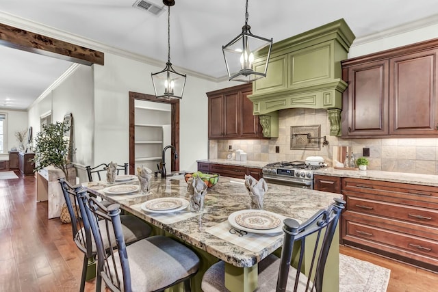 kitchen featuring stainless steel gas range oven, visible vents, ornamental molding, dark wood-style floors, and light stone countertops