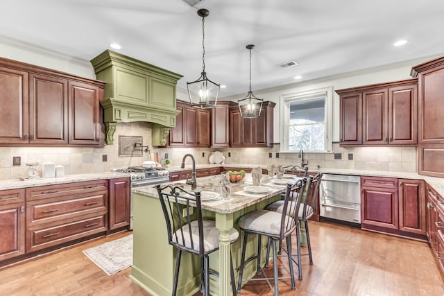 kitchen featuring visible vents, stainless steel gas stove, a kitchen island with sink, light stone counters, and wood finished floors