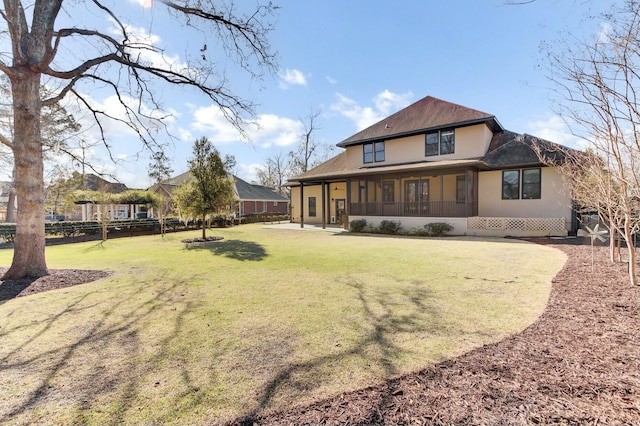 rear view of property with fence, a lawn, and stucco siding