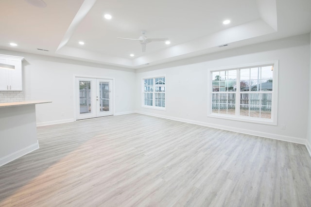 unfurnished living room with french doors, a tray ceiling, light wood-type flooring, and ceiling fan