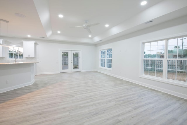 unfurnished living room with a tray ceiling, a healthy amount of sunlight, and light hardwood / wood-style flooring