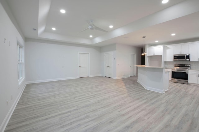 kitchen featuring appliances with stainless steel finishes, backsplash, white cabinetry, pendant lighting, and light hardwood / wood-style flooring