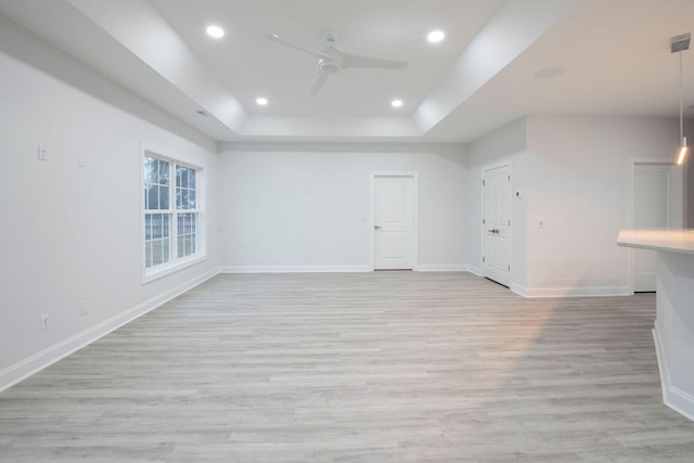 empty room with light hardwood / wood-style floors, a raised ceiling, and ceiling fan