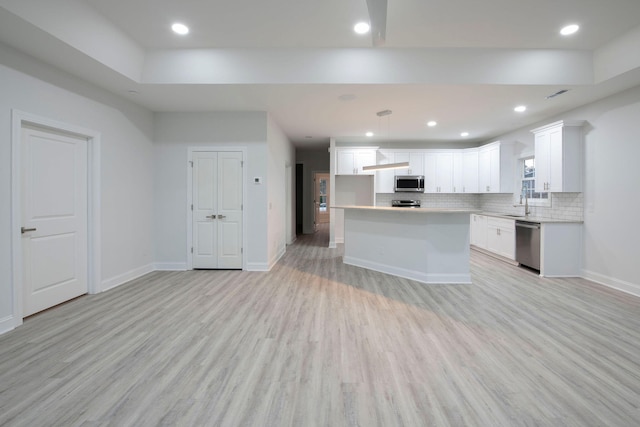 kitchen featuring a kitchen island, white cabinetry, light hardwood / wood-style flooring, decorative light fixtures, and stainless steel appliances