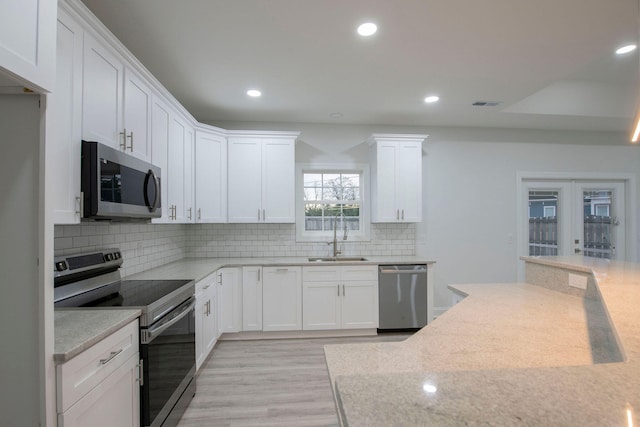 kitchen with sink, light stone countertops, light wood-type flooring, white cabinetry, and appliances with stainless steel finishes