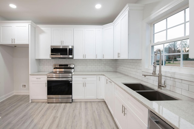 kitchen featuring stainless steel appliances, sink, white cabinets, light stone counters, and light hardwood / wood-style floors