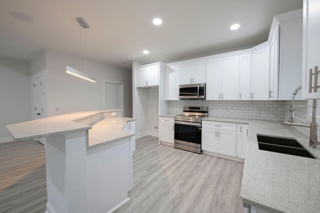 kitchen featuring appliances with stainless steel finishes, white cabinetry, light wood-type flooring, sink, and decorative light fixtures