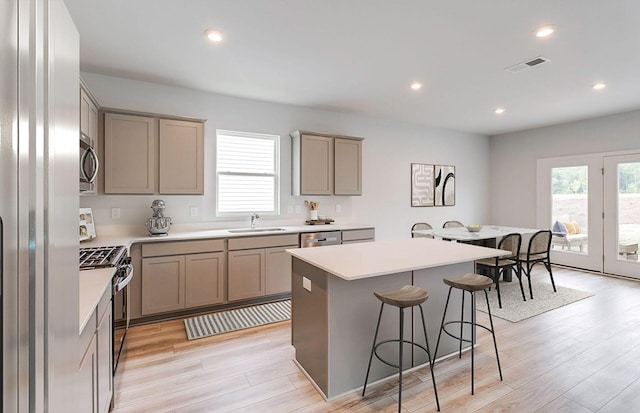 kitchen with sink, a kitchen island, appliances with stainless steel finishes, a kitchen breakfast bar, and light hardwood / wood-style floors