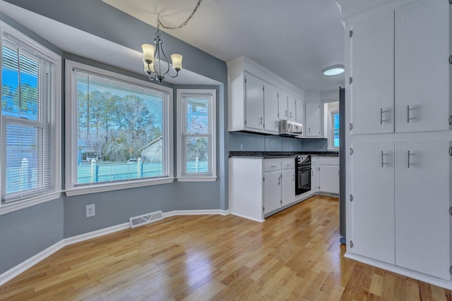 kitchen with oven, visible vents, white cabinetry, hanging light fixtures, and stainless steel microwave