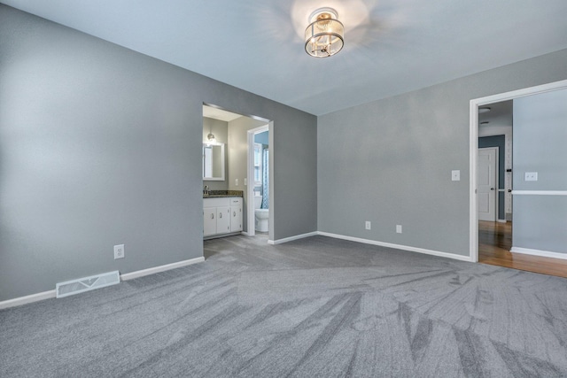 unfurnished bedroom featuring carpet floors, baseboards, visible vents, and ensuite bathroom