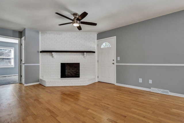 unfurnished living room featuring a healthy amount of sunlight, a brick fireplace, light wood-type flooring, and visible vents