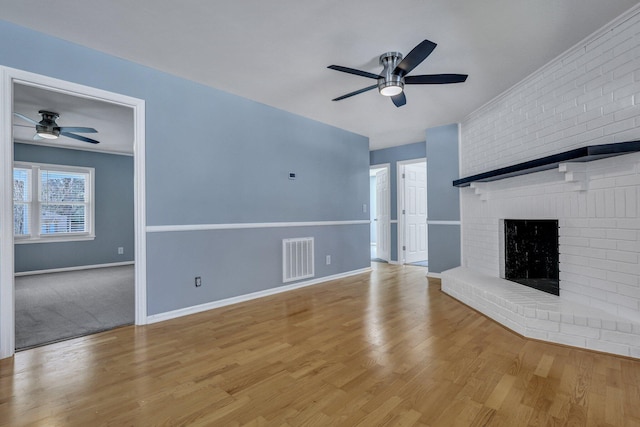 unfurnished living room with a ceiling fan, visible vents, baseboards, a brick fireplace, and light wood finished floors