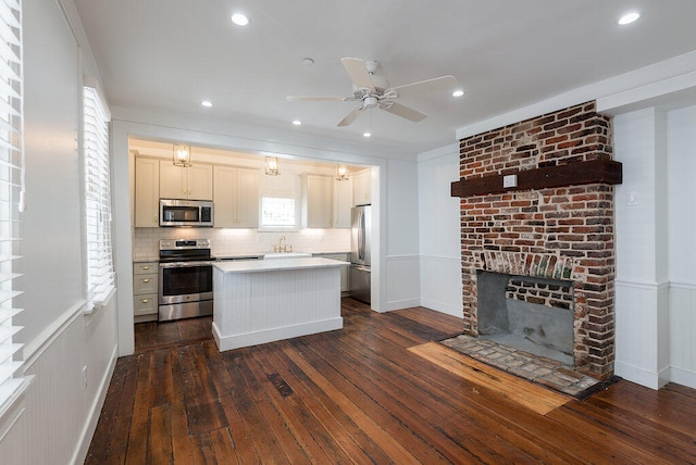 kitchen featuring backsplash, appliances with stainless steel finishes, dark hardwood / wood-style floors, a center island, and a fireplace