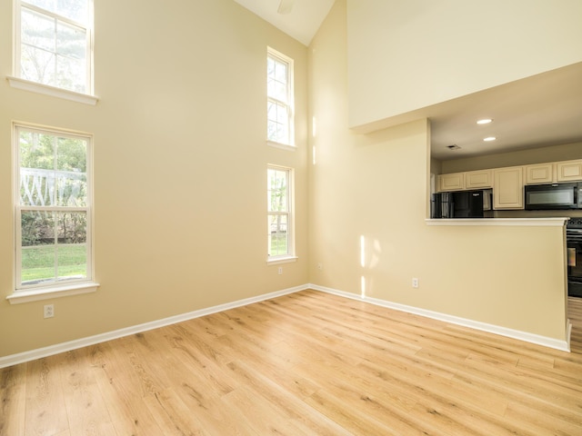 unfurnished living room featuring light wood-style floors, a towering ceiling, and a healthy amount of sunlight