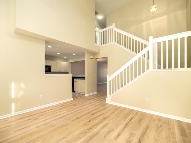 unfurnished living room with a towering ceiling, light wood-type flooring, baseboards, recessed lighting, and stairs
