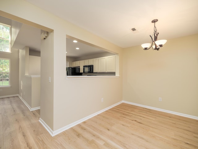 empty room with a wealth of natural light, visible vents, light wood-type flooring, and an inviting chandelier