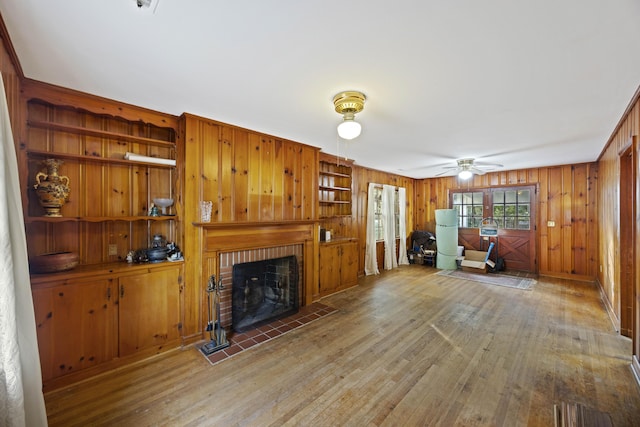 living room with hardwood / wood-style flooring, ceiling fan, a fireplace, and wood walls