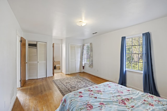 bedroom with connected bathroom, two closets, and hardwood / wood-style flooring