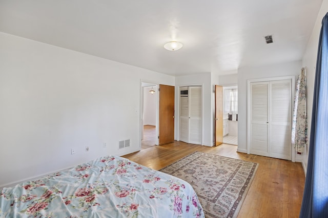 bedroom featuring connected bathroom, two closets, and wood-type flooring