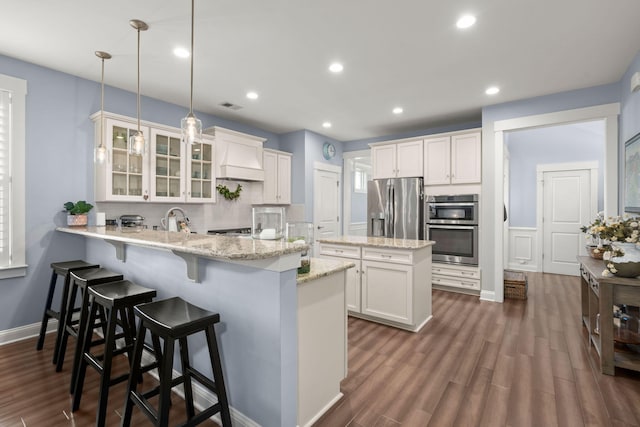 kitchen featuring stainless steel appliances, kitchen peninsula, pendant lighting, white cabinets, and custom exhaust hood