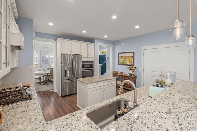 kitchen with pendant lighting, white cabinets, sink, light stone countertops, and stainless steel appliances