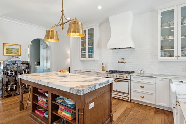 kitchen with stainless steel range, decorative light fixtures, white cabinets, custom exhaust hood, and light wood-type flooring