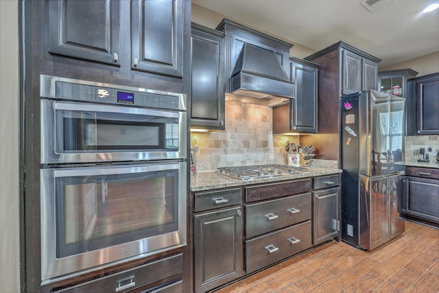 kitchen with backsplash, stainless steel appliances, light hardwood / wood-style floors, and custom exhaust hood