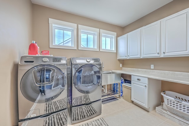 laundry room featuring washing machine and dryer, light tile patterned floors, and cabinets