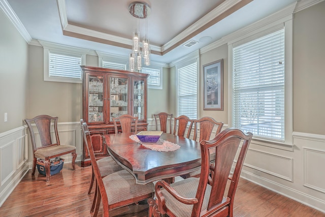 dining space featuring an inviting chandelier, a raised ceiling, crown molding, and wood-type flooring