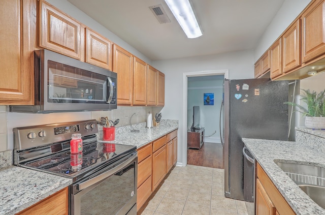 kitchen featuring tasteful backsplash, light stone countertops, light tile patterned floors, and appliances with stainless steel finishes