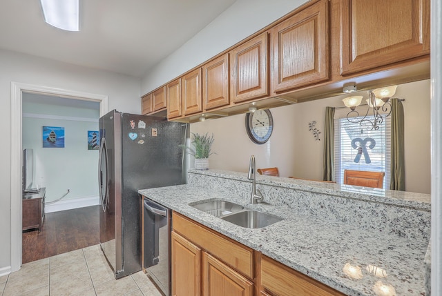 kitchen with appliances with stainless steel finishes, light wood-type flooring, light stone counters, sink, and a chandelier