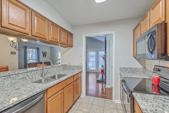 kitchen featuring appliances with stainless steel finishes, light wood-type flooring, light stone counters, and sink