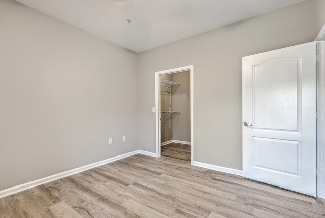 unfurnished bedroom featuring a walk in closet, a closet, and light wood-type flooring