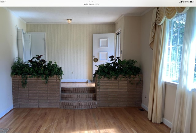 interior space featuring wallpapered walls, ornamental molding, wood finished floors, and baseboards