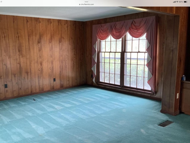 carpeted spare room with wood walls, visible vents, a wealth of natural light, and ornamental molding