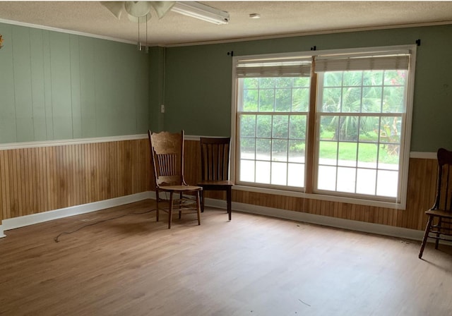 living area with wood walls, crown molding, a textured ceiling, and wood finished floors