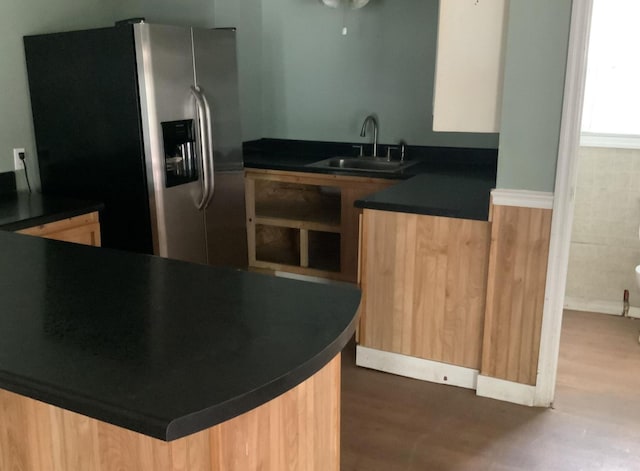 kitchen with wood finished floors, a sink, modern cabinets, dark countertops, and stainless steel fridge