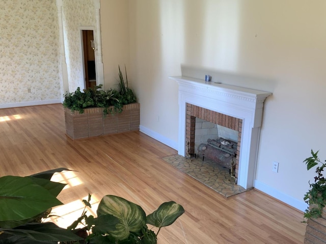 unfurnished living room featuring a brick fireplace, wallpapered walls, baseboards, and wood finished floors