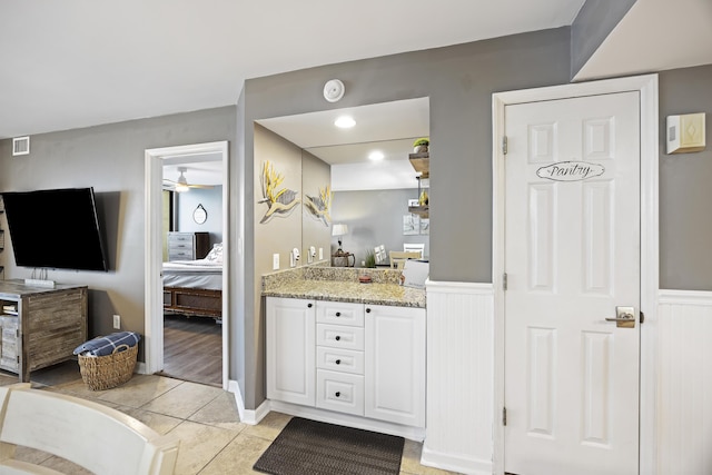 ensuite bathroom with vanity, a wainscoted wall, tile patterned floors, and a ceiling fan