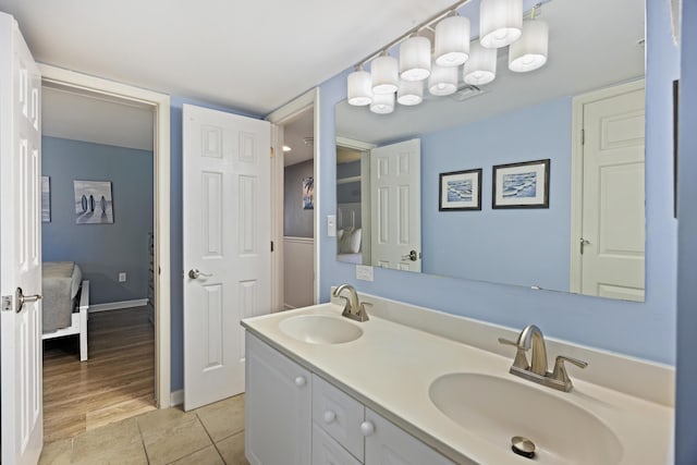 ensuite bathroom featuring double vanity, tile patterned floors, and baseboards