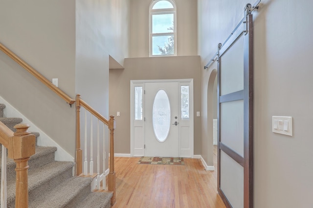 entryway with baseboards, a high ceiling, stairs, a barn door, and light wood-type flooring