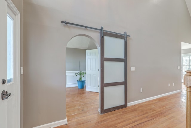 empty room with baseboards, light wood-type flooring, and arched walkways