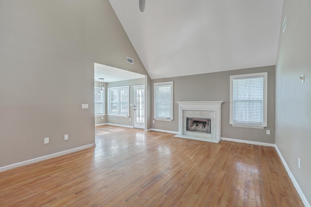 unfurnished living room with a high end fireplace, visible vents, baseboards, light wood-type flooring, and high vaulted ceiling