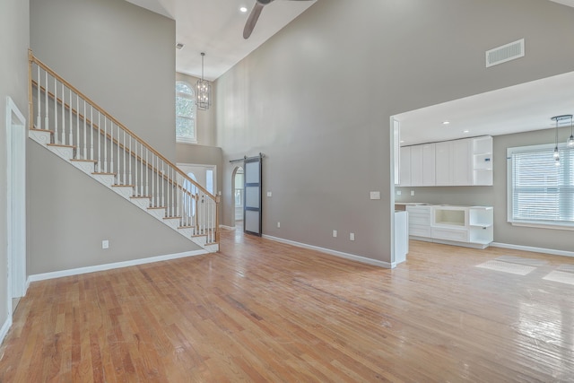 unfurnished living room with visible vents, baseboards, stairs, light wood-style floors, and a barn door