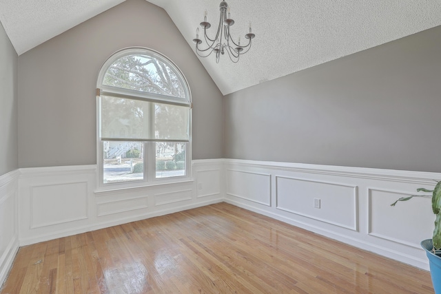 unfurnished room featuring an inviting chandelier, light wood-style floors, lofted ceiling, and a textured ceiling