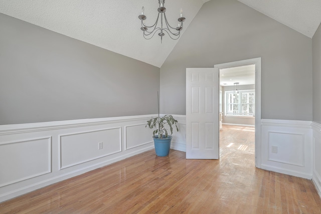 unfurnished room with a textured ceiling, an inviting chandelier, light wood-style flooring, and wainscoting